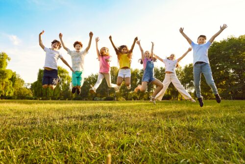 Group of happy children jumping and cheering outdoors on grass